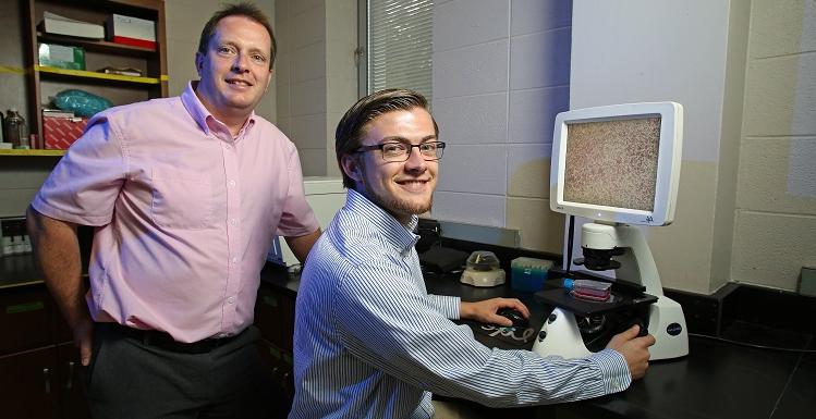 小亚历克斯·科利(左)和博士. Glen Borchert是越来越多的美国本科生和教师合作进行跨学科研究的一员. Coley和Borchert使用这种显微镜观察胰腺癌细胞.