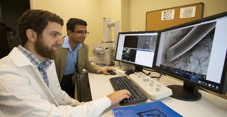 工程系学生优素福·奥马尔(右)和奥马尔博士. 苏米特Arora, 工程学院核心设施的讲师, 用大学的扫描电子显微镜检查放大200倍的银线.  银纳米粒子是他们研究防晒霜和其他生物医学应用的关键成分.