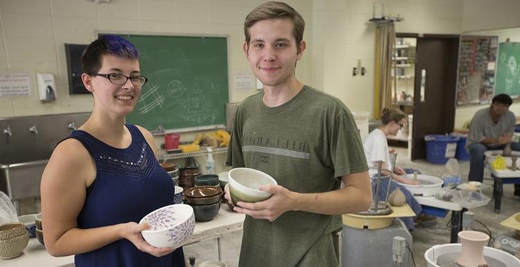 Eric Jager展示了一些由美国为艺术汤制作和捐赠的汤碗, 视觉艺术专业, 还有阿兰娜·克鲁斯, 陶瓷实验室助理.